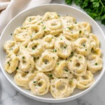 Creamy Tortellini Sauce with golden pasta in glossy cheese sauce on a white plate