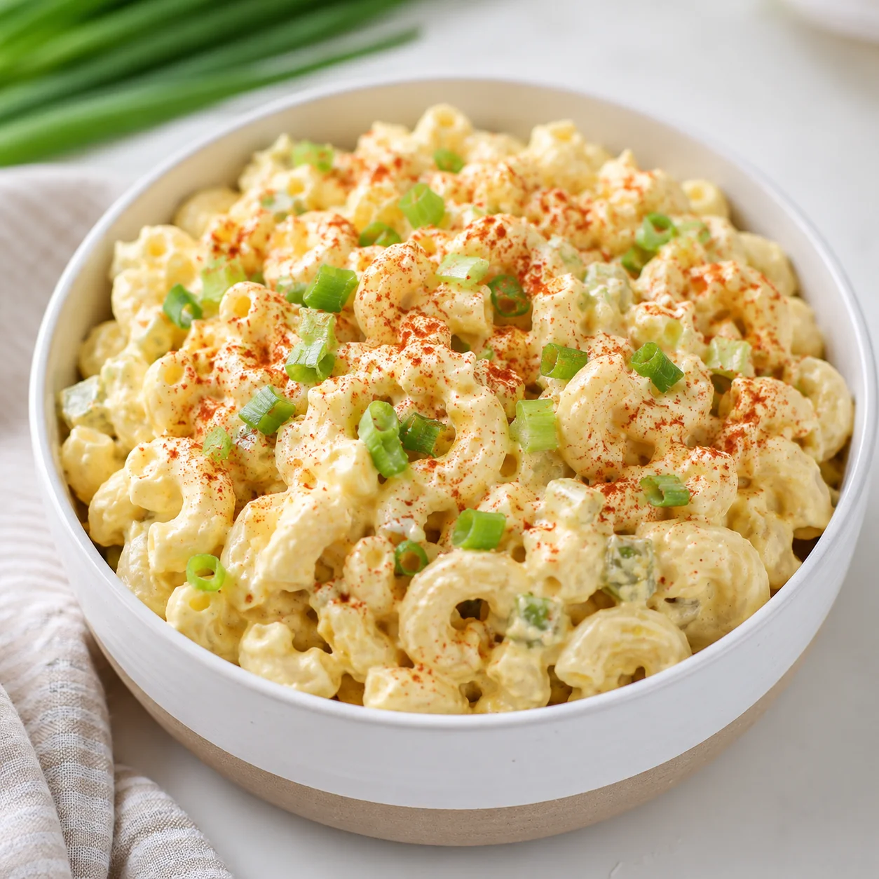 Creamy Deviled Egg Pasta Salad with paprika dusted elbows and green onions in a white bowl