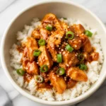 Slow Cooker Honey Garlic Chicken with glossy sauce, scallions, and sesame seeds over rice
