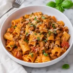 Spicy Italian Sausage Pasta with orange tomato cream sauce and basil in a white bowl