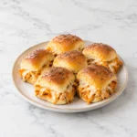 Buffalo chicken sliders with golden buns, saucy shredded chicken, and melted cheese on a modern ceramic plate, centered on a clean white marble surface.